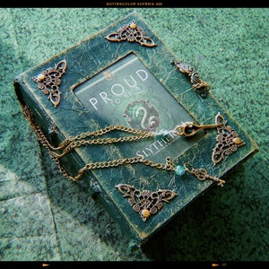 May include: A green book with a gold chain and key charm. The book has a decorative frame with ornate metal corners and a title that reads "Proud to be a Slytherin".