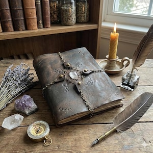 May include: A vintage-style, brown leather book with a chain clasp and a central crystal. A lit candle, a quill, and a compass are on a wooden table, with crystals and lavender. The book features embossed symbols.