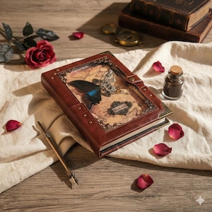 May include: A brown leather journal with a butterfly design on the cover, featuring a blue butterfly and a decorative metal butterfly. The journal is open, revealing a map-like background. A vintage pen and rose petals are nearby.