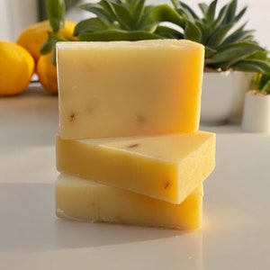 May include: Three bars of handmade soap stacked on top of each other. The soap is a pale yellow color and has a slightly textured surface.