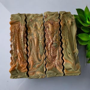 May include: Four bars of handmade soap with a green and brown swirl pattern and gold glitter. The soap is arranged in a row.