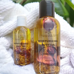 May include: Two glass bottles of moisturizing body oil with dried flowers inside. The bottles are labeled "Hayberwood Beyond Natural LLC" and "Moisturizing Body Oil". The larger bottle is 4 oz.