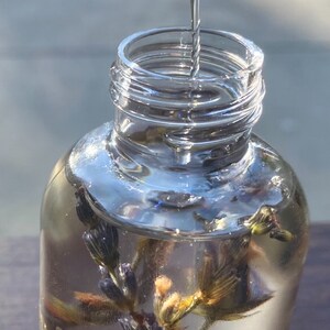 Pu&ograve; includere: Una bottiglia di vetro trasparente con una superficie testurizzata viene riempita con un liquido trasparente. La bottiglia contiene fiori di lavanda secchi. L'etichetta sulla bottiglia recita "Hayberwood Beyond Natural Roman Chamomile"