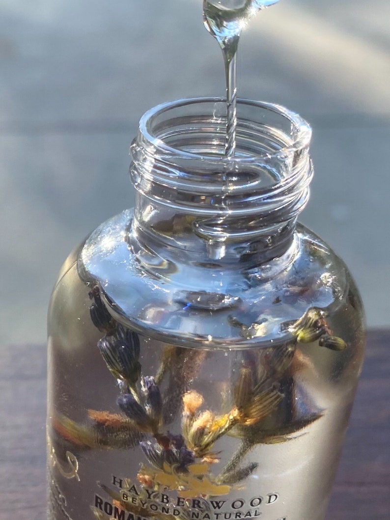 Pu&ograve; includere: Una bottiglia di vetro trasparente con una superficie testurizzata viene riempita con un liquido trasparente. La bottiglia contiene fiori di lavanda secchi. L'etichetta sulla bottiglia recita "Hayberwood Beyond Natural Roman Chamomile"
