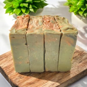 May include: Four bars of handmade soap with a green and brown swirl pattern. The soap is sitting on a wooden surface.