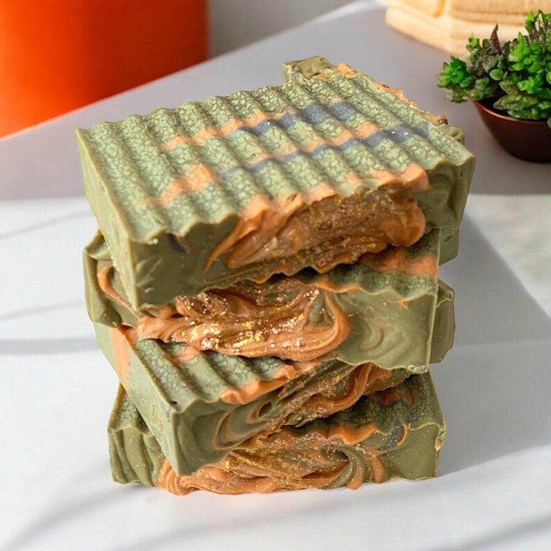 May include: A stack of four handmade soap bars with a green, orange, and gold swirl design. The soap bars have a textured surface.
