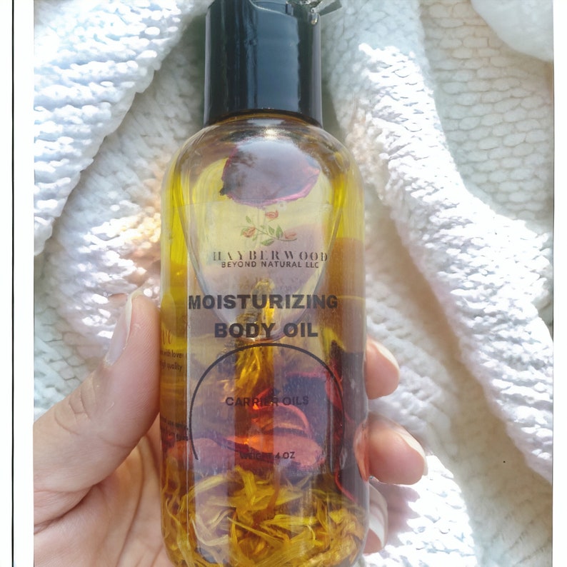May include: A clear glass bottle with a black cap filled with a yellow liquid and dried rose petals. The bottle label reads "Hayberwood Beyond Natural LLC Moisturizing Body Oil Carrier Oils 4 oz."