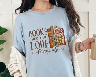 May include: A light blue t-shirt with the text "BOOKS are my LOVE language" and a stack of books with a rose on top.