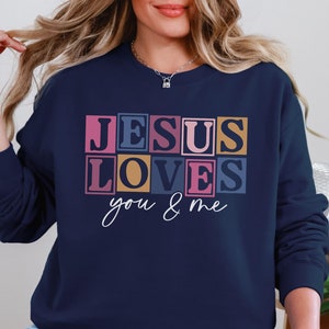 Könnte beinhalten: Navyblauer Pullover mit dem Text "JESUS LOVES you & me" in bunten Blockbuchstaben.