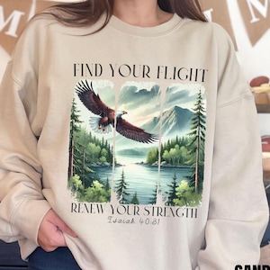 Op de afbeelding: Beige sweatshirt met een afbeelding van een adelaar die over een meer en bergen vliegt. De tekst "Find Your Flight" en "Renew Your Strength Isaiah 40:31" staat op de sweatshirt gedrukt.