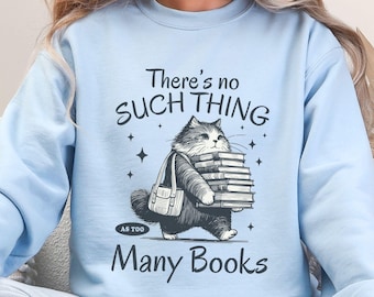 May include: Light blue sweatshirt with the text "There's no SUCH THING as TOO Many Books." A cartoon cat carries a stack of books and a bag. The sweatshirt is a solid light blue color.