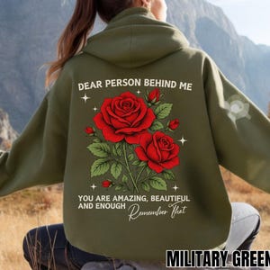 Op de afbeelding: Een militair groene hoodie met een achteropdruk van twee rode rozen met groene bladeren en kleine witte sterren. De tekst in wit en geel luidt: DEAR PERSON BEHIND ME YOU ARE AMAZING, BEAUTIFUL AND ENOUGH Remember That.
