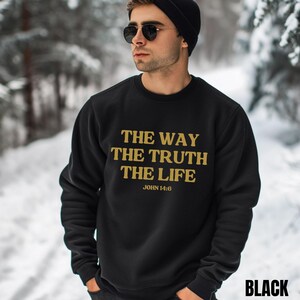 May include: Black sweatshirt with gold text that reads "THE WAY THE TRUTH THE LIFE" and "JOHN 14:6". The word "BLACK" is printed in white at the bottom right. The sweatshirt is worn by a person wearing a black beanie and sunglasses.