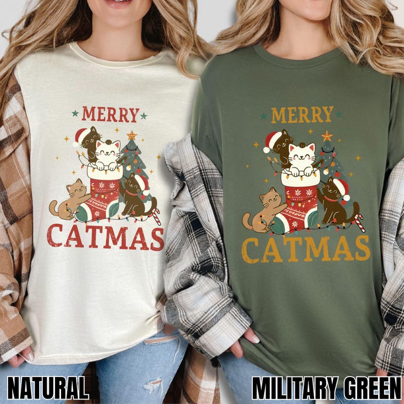 Op de afbeelding: Twee T-shirts, &eacute;&eacute;n in naturel en &eacute;&eacute;n in legergroen, tonen een "Catmas"-ontwerp. Het ontwerp bevat katten, een kerstboom en een sok. De tekst "Merry Catmas" staat boven en onder de afbeelding.