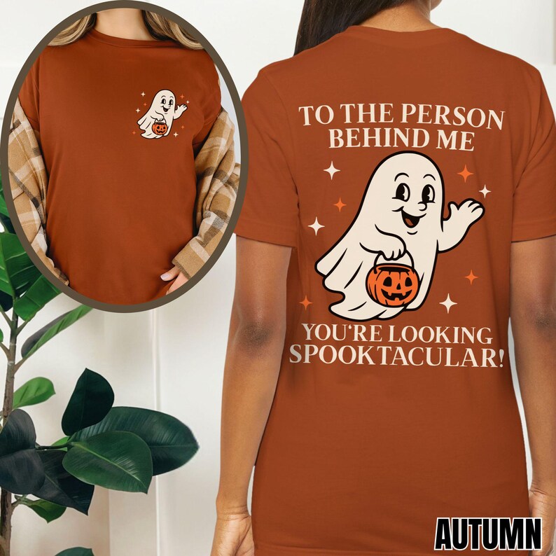 Puede incluir: Una camiseta color &oacute;xido con un gr&aacute;fico de un fantasma blanco sosteniendo una calabaza naranja. La parte posterior muestra el texto: TO THE PERSON BEHIND ME YOU'RE LOOKING SPOOKTACULAR! El pecho muestra una versi&oacute;n m&aacute;s peque&ntilde;a del mismo gr&aacute;fico.