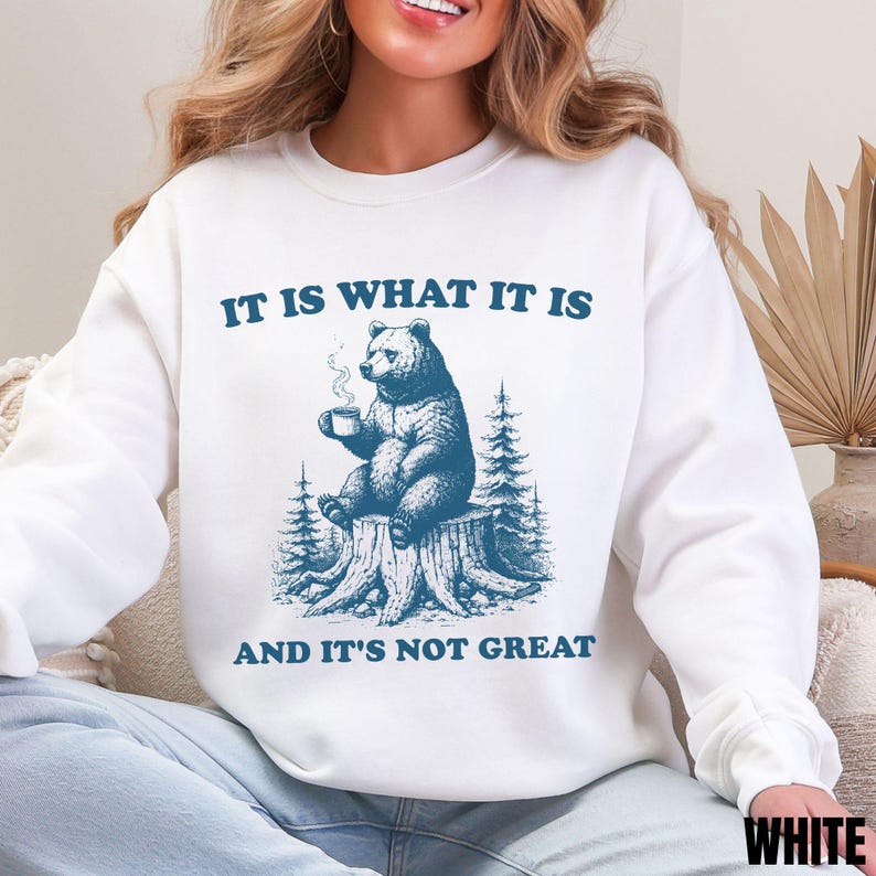White sweatshirt with a blue vintage cartoon animal design and the phrase 'It Is What It Is and It’s Not Great' – funny anxiety-themed mental health shirt for adults."