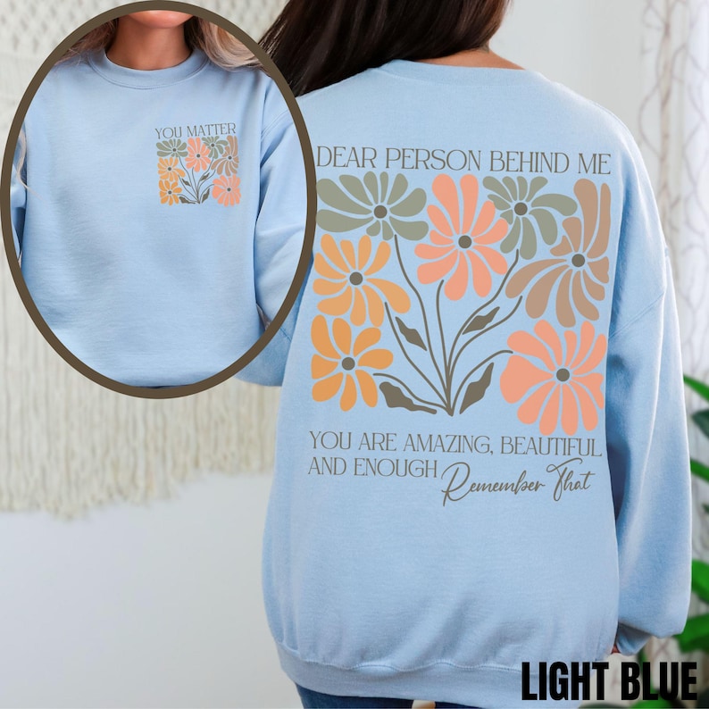 Puede incluir: Sudadera azul claro con un dise&ntilde;o floral y el texto "Querida persona detr&aacute;s de m&iacute;, eres incre&iacute;ble, hermosa y suficiente. Recuerda eso." en la espalda. La parte delantera de la sudadera tiene el texto "Importas" con un peque&ntilde;o dise&ntilde;o floral.