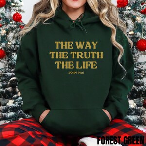 May include: Forest green hoodie with the text "THE WAY THE TRUTH THE LIFE JOHN 14:6" in gold lettering. The hoodie has a drawstring hood and a front pocket. The bottom of the hoodie has the text "FOREST GREEN".