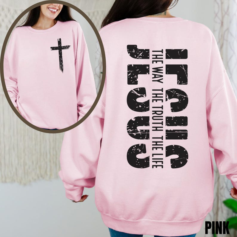 May include: Pink sweatshirt with a distressed black graphic of the word "Jesus" and the text "The Way, The Truth, The Life" on the back. The front of the sweatshirt has a distressed black cross graphic.