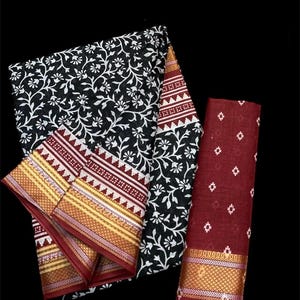 Pu&ograve; includere: Un set di tre pezzi di tessuto di cotone stampato floreale bianco e nero con bordi marroni e dorati. Il tessuto &egrave; piegato e disposto su uno sfondo nero.