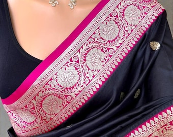 Può includere: Sari nero con un bordo rosa acceso e un intricato ricamo floreale dorato. Il sari presenta un design dettagliato ed è abbinato a un top nero. Una collana di perle aggiunge un tocco di eleganza.