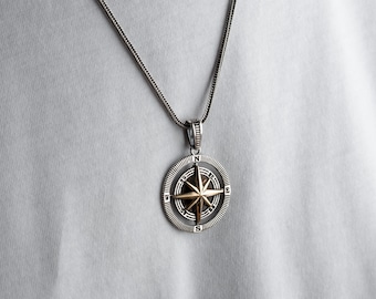 May include: A silver chain necklace with a compass pendant. The compass is round and has a gold-colored center with a star design.