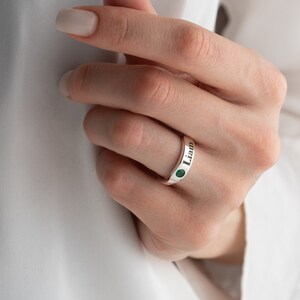 May include: A silver ring engraved with the name "Liam". The ring features a small green gemstone set into the band.