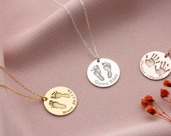 May include: Three silver necklaces with personalised pendants. The pendants feature a handprint, a footprint, and two footprints. The handprint pendant says "Raphael Amalia" and the footprint pendants say "Quinn Riley" and "Bruno 06.17.19".
