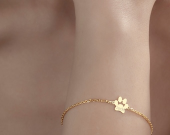 Puede incluir: Un brazalete de cadena dorada con un pequeño dije en forma de huella de pata grabado con el nombre "Jack".