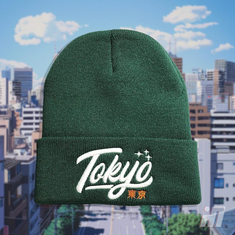 May include: A dark green beanie with a white embroidered logo that says "Tokyo" in a stylized font. The logo also includes the Japanese characters for "Tokyo" in orange.