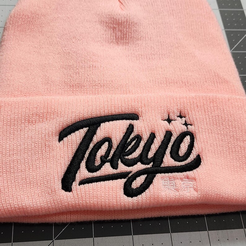 May include: Pink beanie with a black embroidered logo that says "Tokyo" with a star design above the word.