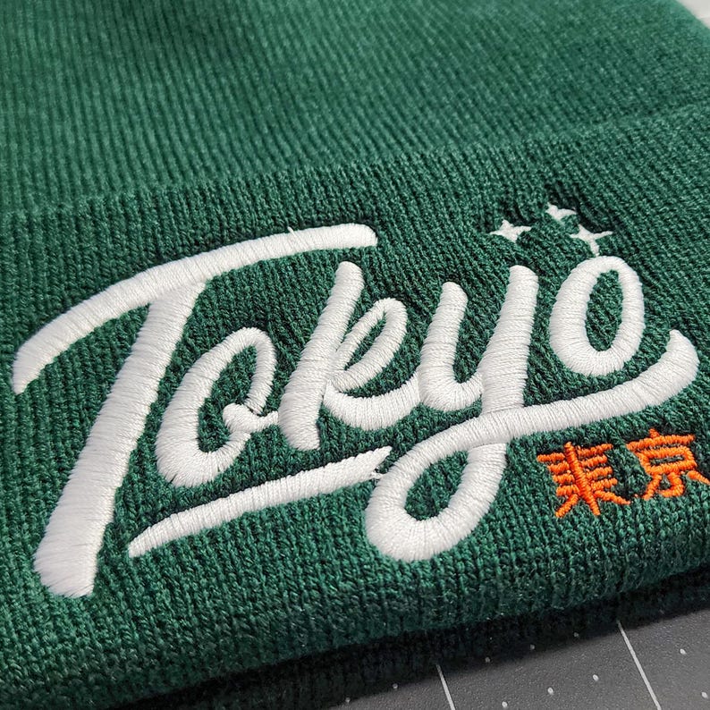 May include: A green beanie with white embroidered text that says "Tokyo" and orange text that says "東京".