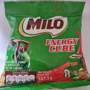Pode incluir: Uma embalagem verde e vermelha de Milo Energy Cubes. A embalagem apresenta o logotipo Milo, um gráfico de uma pessoa jogando basquete e as palavras "Energy Cube". O peso líquido é de 137,5 g.