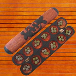 May include: A wooden mancala board game with a dark brown finish, featuring a hinged design and small round pits filled with green and off-white stones. A wooden stick with a black carved design is also included.