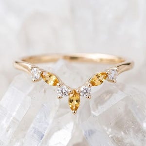 Peut inclure: Une bague en or en forme de V ornée d'une pierre jaune centrale taille marquise, entourée de deux pierres rondes transparentes, avec d'autres pierres jaunes taille marquise et rondes transparentes disposées symétriquement sur l'anneau.