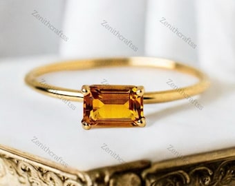 May include: A gold ring with a rectangular, orange gemstone. The ring is simple and elegant.