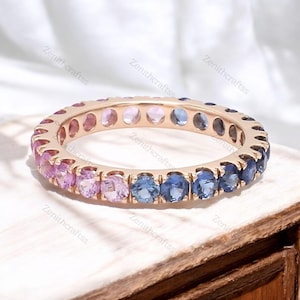 May include: A gold band ring set with a rainbow of sapphires. The ring features pink, blue and purple sapphires.