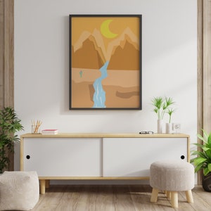 May include: A framed print of a desert landscape with a waterfall and a crescent moon in the sky. The print is in a black frame and is hanging on a white wall.