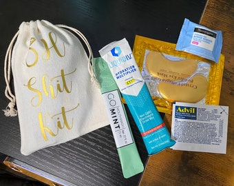May include: A white canvas bag with the text "SH Shit Kit" in gold lettering. The bag contains a variety of items, including a blue and green electrolyte drink mix packet, a blue and green mouthwash packet, a gold eye mask, and a packet of Advil pain relief tablets.