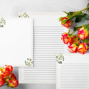 May include: White stationery with eucalyptus accents and lined pages. A bouquet of orange and yellow roses with green leaves is arranged on the side. The stationery is perfect for writing letters or notes.