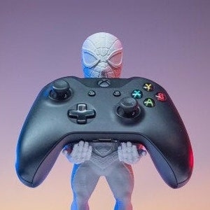 May include: A white and black Spider-Man figurine holding a black Xbox controller. The figurine is standing on a round base.
