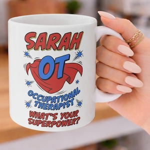 Peut inclure: Mug en céramique blanche avec le nom "Sarah" en rouge et jaune, et "OT" en bleu, avec un motif de cape rouge. Le texte "Occupational Therapist" et "What's Your Superpower?" sont également affichés.
