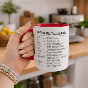 Peut inclure: Un mug en céramique blanc avec un intérieur et une anse rouges, portant le texte noir 60 Year Old Texting Code. La liste présente des définitions humoristiques pour des acronymes comme ATD pour At The Doctor, BFF pour Best Friend Fell et TTYL pour Talk To You Louder.