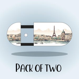 May include: A pair of USB flash drives with a Parisian cityscape design. The illustration features the Eiffel Tower, buildings, and a river. The text "PACK OF TWO" is below the drives.