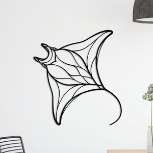 May include: Black metal wall art sculpture of a manta ray, hanging on a white wall above a wooden table with black chairs. The table is decorated with three glass vases filled with white flowers.