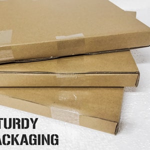 Może przedstawiać: Trzy brązowe kartony ułożone jeden na drugim. Kartony są zaklejone taśmą i mają napis "STURDY PACKAGING" nadrukowany na dolnym kartonie.