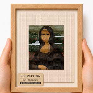 May include: A cross-stitch embroidery of the Mona Lisa in a light wood frame. The artwork features a pixelated portrait in shades of brown, green, and black. A label at the bottom reads: PDF PATTERN, 32 x 40 stitches, INSTANT DOWNLOAD.