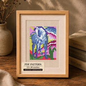 Puede incluir: Un marco de madera clara que contiene un patrón de punto de cruz de un caballo azul sobre un fondo geométrico colorido. Una etiqueta en la parte inferior dice PDF PATTERN, 32 x 40 stitches, INSTANT DOWNLOAD. El diseño presenta tonos azules, rosas y verdes.