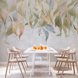 May include: A dining room with a white table and six wooden chairs. The wall behind the table features a wallpaper mural of watercolor leaves in shades of green, blue, and orange.