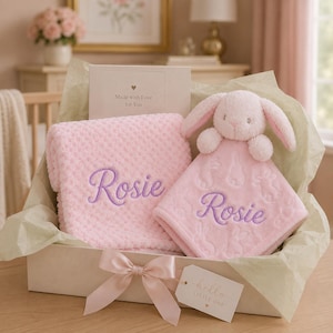 Può includere: Un set regalo contenente una coperta rosa chiaro testurizzata e un doudou a forma di coniglietto abbinato, entrambi ricamati con il nome Rosie in corsivo viola. Un biglietto riporta Made with Love for You e un'etichetta dice hello LITTLE ONE.